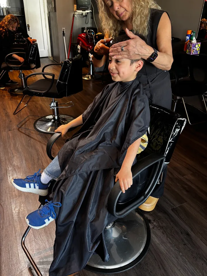 A boy in a black cape mid-haircut in a salon chair